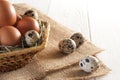 Chicken and quail eggs in basket and on burlap. White background.