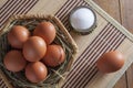 Large brown chicken eggs and variegated quail eggs lie on straw in a wicker basket on a wooden table. Royalty Free Stock Photo