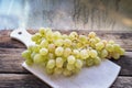 Large brush of grapes in a wooden cup, old wooden table white cutting board Royalty Free Stock Photo