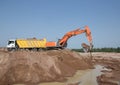 large bucket of an orange crawler excavator pours earth into a yellow dump truck