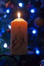 A large candle burns against the background of a garland with shining lights. Vertical photo, defocus. Mystic esoteric romance