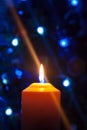 A large candle burns against the background of a garland with shining lights. Vertical photo, defocus. Mystic esoteric romance