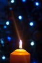A large candle burns against the background of a garland with shining lights. Vertical photo, defocus. Mystic esoteric
