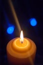 A large candle burns against the background of a garland with shining lights. Vertical photo, defocus. Mystic esoteric