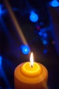 A large candle burns against the background of a garland with shining lights. Vertical photo, defocus. Mystic esoteric romance