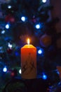 A large candle burns against the background of a garland with shining lights. Vertical photo, defocus. Mystic esoteric romance
