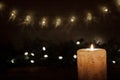 A large candle burns in the dark on a black background. Garland lights and stars. Christmas and New Year