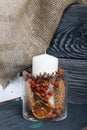 A large candle in a glass vessel. Cones, mountain ash, anise stars, cinnamon sticks are poured into it for decoration. Stands on