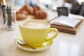 Large cappuccino coffee in yellow cup and saucer on counter