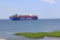 Large cargo ship cosco shipping navigates through the sea along the green salt marsh in summer