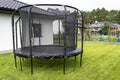 Large childrens jumping trampoline with protective net and closed zipper, standing in the garden.
