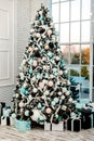 Large Christmas tree with gifts in blue boxes near the large window