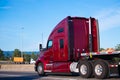 Big rig dark red semi truck tractor driving with flat bed trailer on the road Royalty Free Stock Photo