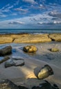 Large colourful rocks in calm shallow sea water soft waves blue sky with clouds