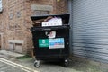 Overflowing commercial waste bin rear of shops