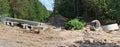 Large concrete beams and pipes heaps of sand with traces of heavy equipment wheels on a construction site in the forest