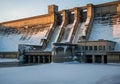 Massive concrete dam with water flowing over spillways, partially covered in snow and ice during winter Royalty Free Stock Photo