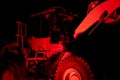 Large construction vehicle with rugged tires and a raised loader arm illuminated by intense red lighting Royalty Free Stock Photo