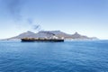 Large container ship at sea in front of Cape Town and Table Mountain. Vessel emitting black exhaust smoke from funnel