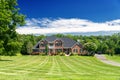 Large country brick house and summer landscape with a perfect lawn. Blue sky and white clouds