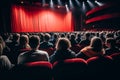 A large crowd of theatre goers sitting in comfortable red seats waiting for the show to start in front of a big red curtain