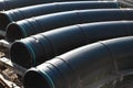 Large diameter black gasification pipes lie in a row in an open warehouse on the street on a summer day. Royalty Free Stock Photo