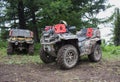 Large dirt-covered ATVs stand in a coniferous forest