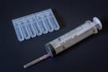 A large disposable syringe and a package of plastic ampoules lie on a black background.