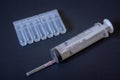 A large disposable syringe and a package of plastic ampoules lie on a dark background.