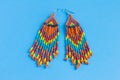 Large earrings made of multi-colored beads and bugle beads, boho style, on a blue background Royalty Free Stock Photo