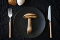 A large edible mushroom lies on a black plate next to the cutlery