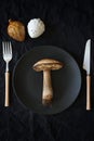 A large edible mushroom lies on a black plate next to the cutlery