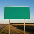 Blank green roadside sign standing tall against a clear blue sky with a rural landscape background Royalty Free Stock Photo