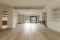 Large empty living room with custom wooden shelving on the walls, exposed concrete beams, white oak wooden floors, cream painted