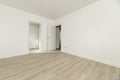 Large empty room with white painted walls, white wooden skirting boards, doors leading to two rooms and white oak wooden floors