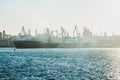 A large empty ship is parked at the top of an industrial base in the sea. The rays of the sun break through the dust