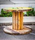 Large Empty Wooden Spool on asphalt, and a white stripped pattern wall in the background. Royalty Free Stock Photo