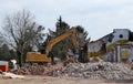 Large excavator on heap of debris demolishes the old house for an urban redevelopment