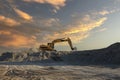 Large excavator working on an industrial site under a sunset sky