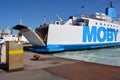 A large ferry has docked in the port and is waiting for passengers and cars with an open ramp