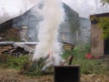 A large fire with smoke burning dry grass in the yard near a wooden house in the fall Royalty Free Stock Photo