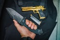 A large folding tactical knife in a manÃ¢â¬â¢s hand against the background of a golden pistol Royalty Free Stock Photo
