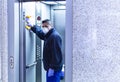 Large format of a male wearing a medical face mask and disinfecting an elevator