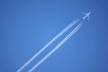 Large four engine passenger supersonic aircraft flying from left to right high in blue cloudless sky leaving long white trail Royalty Free Stock Photo