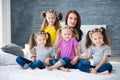 Large friendly family, many children: mom and four pretty cheerful girls triple twins sisters sitting on a bed against a gray Royalty Free Stock Photo