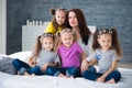 Large friendly family, many children: mom and four pretty cheerful girls triple twins sisters sitting on a bed against a gray Royalty Free Stock Photo