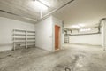 A large garage of a single-family home with white-painted walls, white metal shelves, and dirty polished cement floors