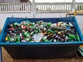 A large garbage bin filled with used glass bottles.