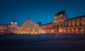 The large glass pyramid and the main courtyard of the Louvre Museum at dusk.