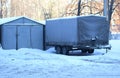 Large gray four-wheeled trailer stands near a metal garage